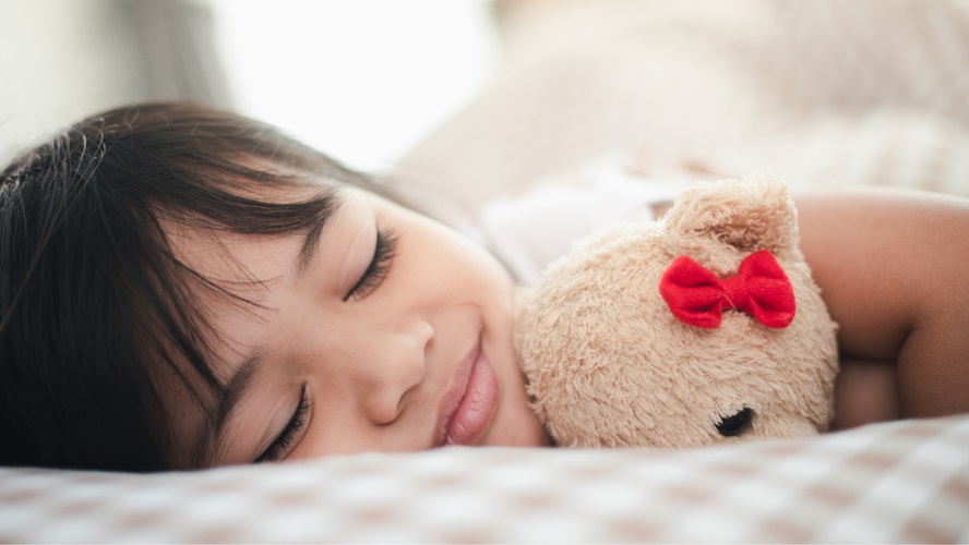 Enfant dormant paisiblement dans son lit avec son doudou ours dans les bras.